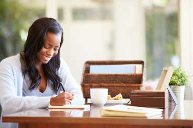 Woman Writing In Notebook Sitting At Desk