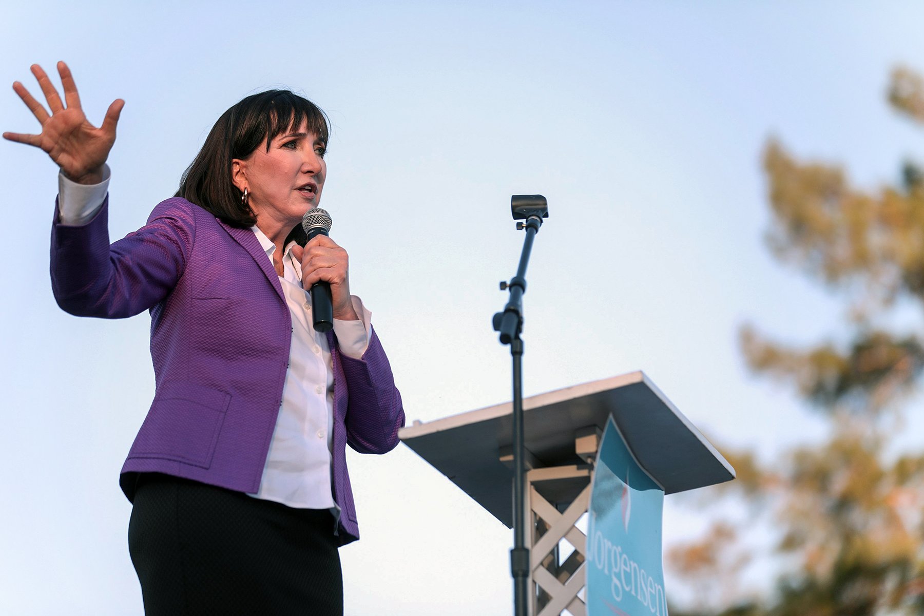 Jo Jorgensen speaking to the microphone in front of a podium outside.