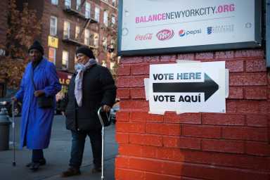 Two ladies walking with canes to voting lcation. "Vote Here/Vote Aqui" sign directing voters to the voting location.