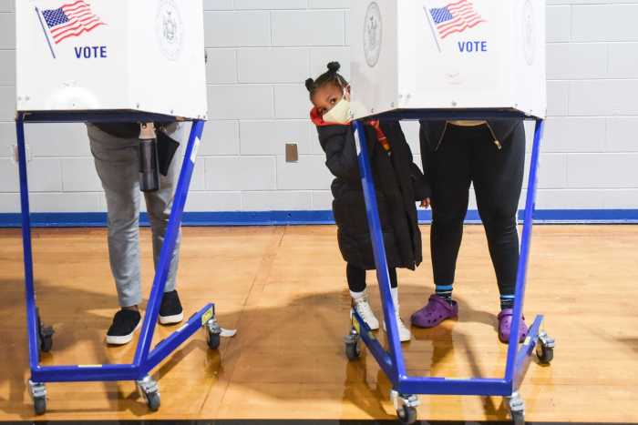 At poll site - a girl looks at the camera as her mother vote in a voting booth.