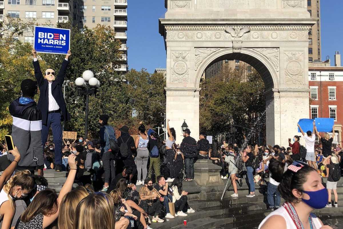 A crowd at Washington Sq park. A man wearing biden mask holding "Biden/Harris" campaign poster