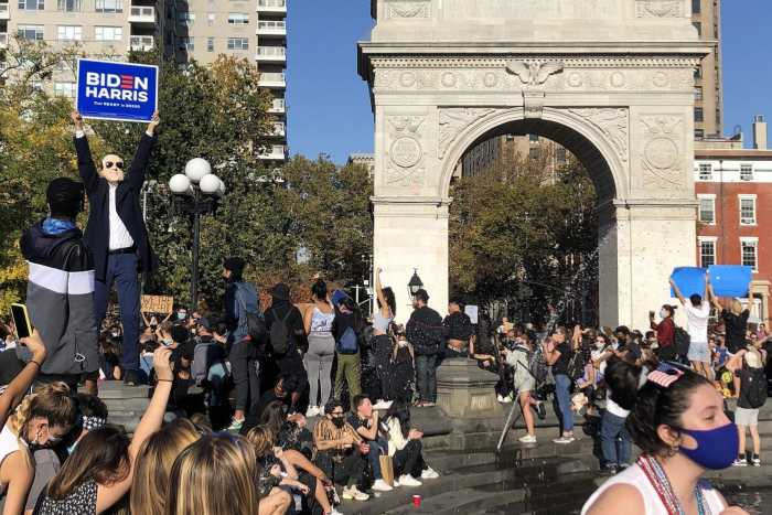 A crowd at Washington Sq park. A man wearing biden mask holding "Biden/Harris" campaign poster