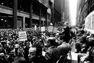 Charles Zimmerman speaks at a civil rights-labor movement rally in the New York Garment District on 38th Street near 7th Avenue in New York City. Signs include "Labor Opposes Discrimination"