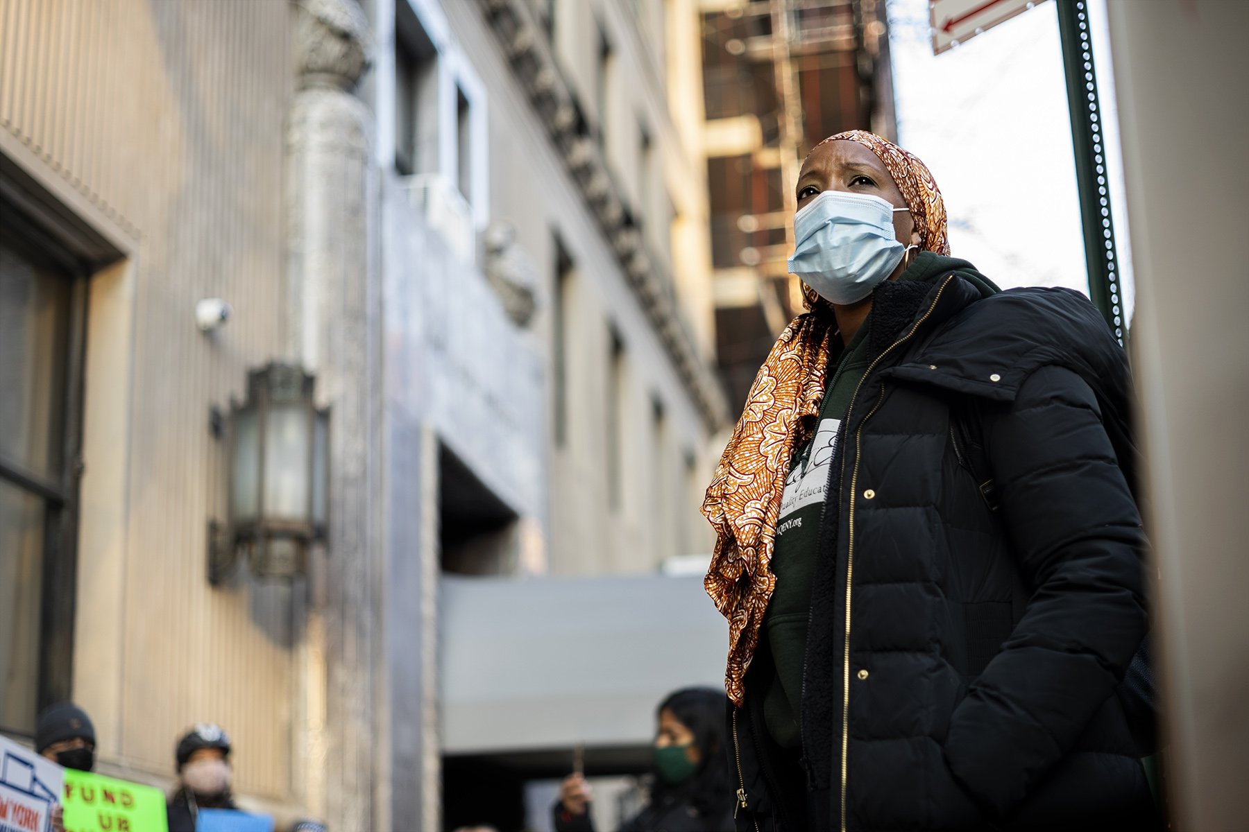 Zakiyah Ansari in front of a line of protesters holding signs in front of 470 Park Ave. building