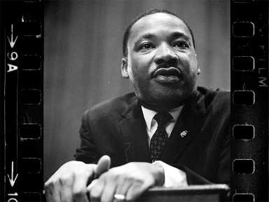 Martin Luther King Jr. holding on to the podium with both hands, looking far.